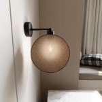 Kinkiet Motif 1xE14 w kolorze czarnym z naturalnym abażurem, o okrągłym kształcie. Montowany na ścianie, z widocznym źródłem światła wewnątrz. Tło jasne, minimalistyczne, z elementami tekstylnymi w aranżacji.
