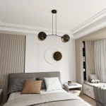 Lampa wisząca Motif 2xE14 marbel z dwoma kulistymi kloszami w kolorze czarnym ze złotym wzorem, zawieszona na cienkich linkach. Produkt umieszczony w nowoczesnej sypialni, nad łóżkiem z pościelą w odcieniach szarości i brązu.