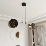 Lampa wisząca Motif 2xE14 w stylu marbel z dwoma okrągłymi kloszami w czerni z złotymi żyłkami, zawieszona na cienkich linkach. Klosze są umieszczone na łukowatej podstawie, w nowoczesnym wnętrzu. Tło z jasnymi ścianami i zasłonami.