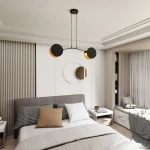 Lampa wisząca Motif 2xE14 w kolorze czarnym i złotym, z dwoma okrągłymi kloszami. Zawieszona na cienkich linkach, umieszczona nad łóżkiem w nowoczesnej sypialni. Tło jasne, z minimalistycznym wystrojem wnętrza.