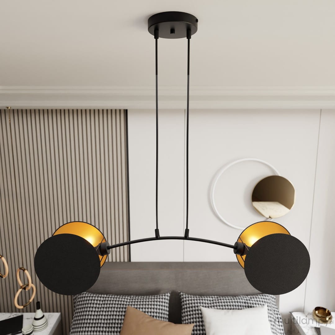 Lampa wisząca Motif z dwoma kloszami, czarna z złotymi akcentami, zawieszona na dwóch smukłych linkach. Klosze mają okrągły kształt, jeden czarny, drugi złoty, w eleganckim wnętrzu nad łóżkiem z poduszkami w kratę.