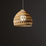 Lampa wisząca Boho S w kolorze białym i rattanowym, z okrągłym kloszem o strukturalnym wzorze. Zawieszona na cienkim, białym przewodzie. Klosz ma kształt przypominający kosz, tworząc efektowne oświetlenie. Tło ciemne, podkreślające detal lampy.