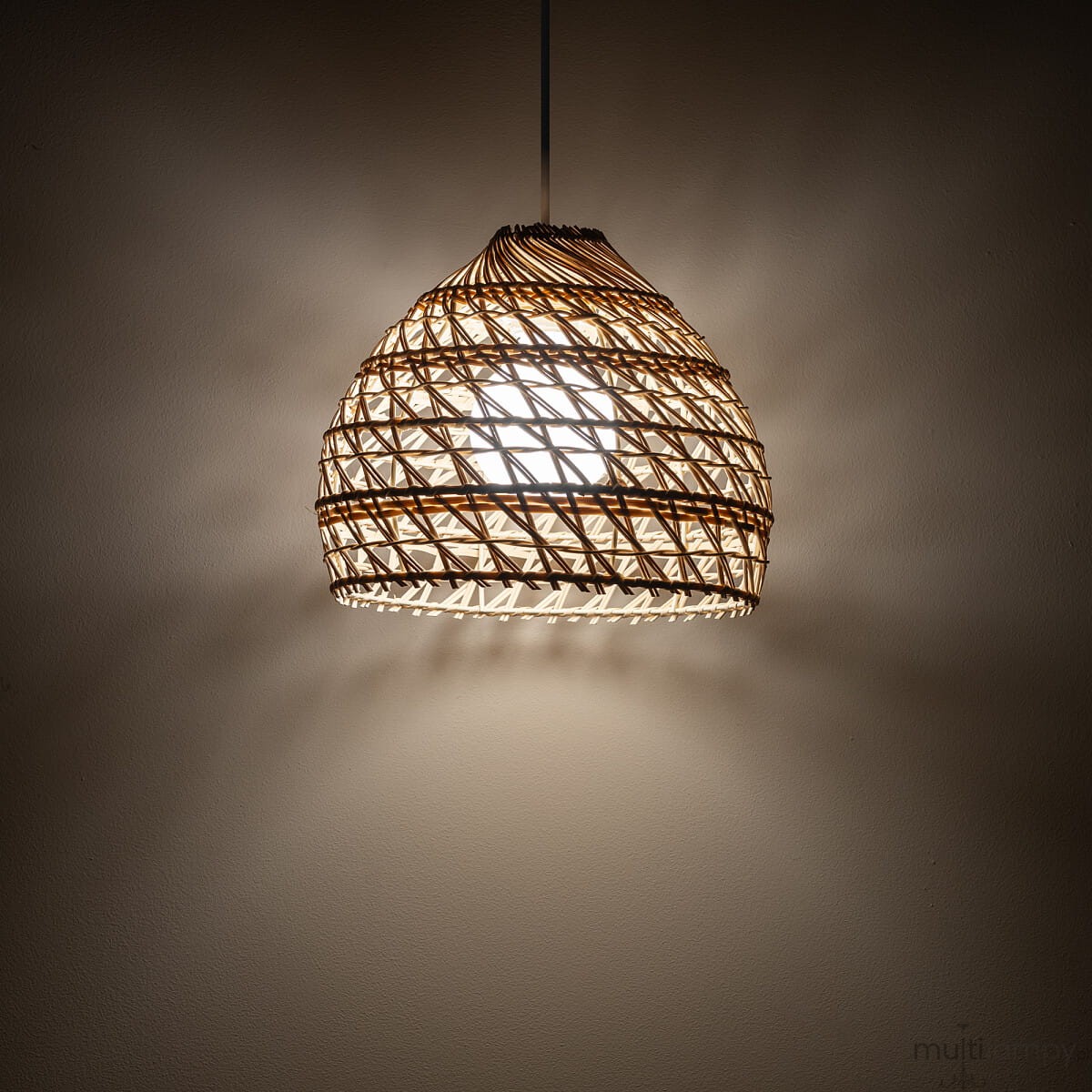 Lampa wisząca Boho S z białym kloszem z rattanu, o kształcie przypominającym kulę, zawieszona na cienkim przewodzie. Wewnątrz znajduje się żarówka E27, emitująca ciepłe światło, które rzuca delikatny cień na ścianę.