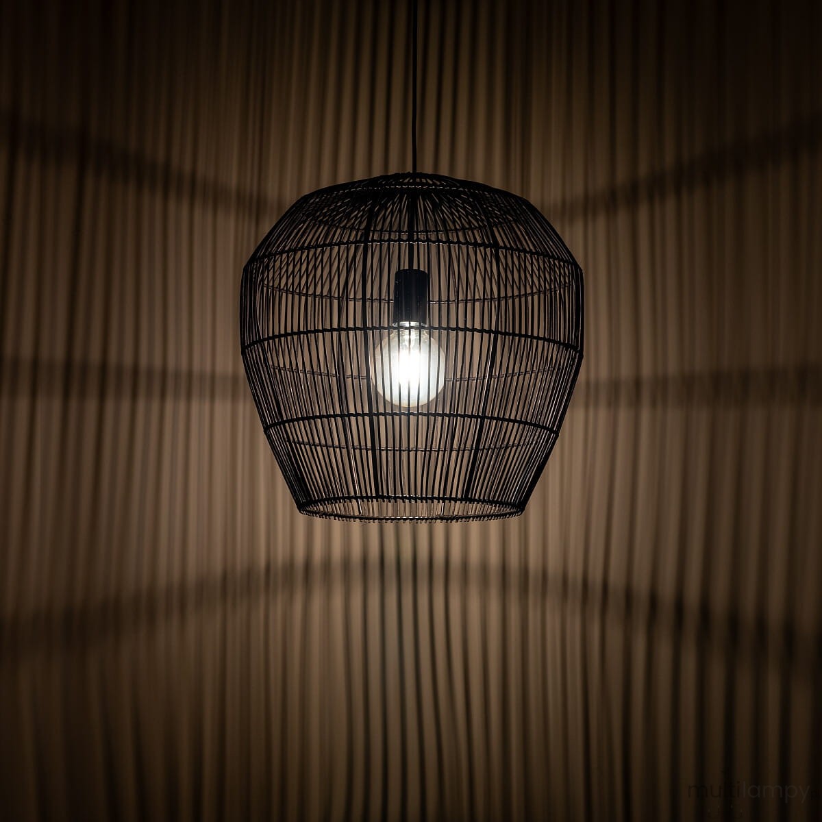 Czarna lampa wisząca Haiti Black S z kloszem w formie metalowej siatki, z widoczną żarówką E27. Zawieszona w górnej części zdjęcia, tworzy delikatne cienie na tle o gładkiej, jasnej fakturze.