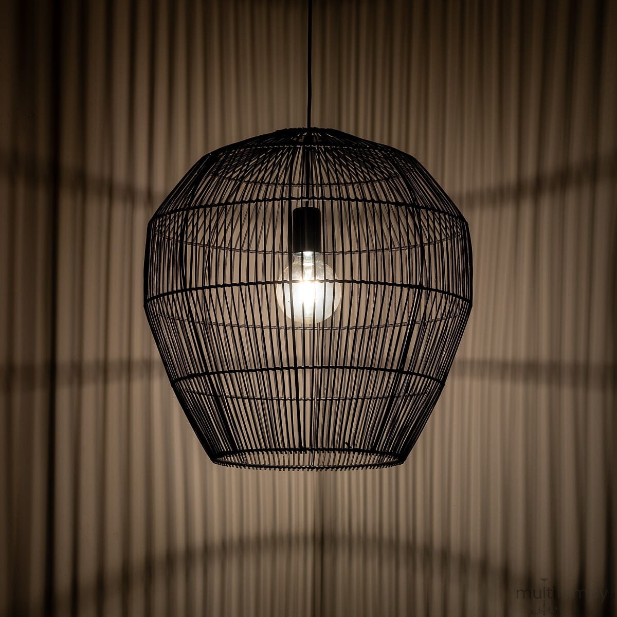 Lampa wisząca Haiti Black M o czarnej metalowej konstrukcji w kształcie owalnym. Zawiera oprawę na żarówkę E27, z widocznym źródłem światła. Produkt zawieszony w górnej części, tworzy ciekawe cienie na tle ściany.