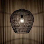 Lampa wisząca Haiti Black M o czarnej metalowej konstrukcji w kształcie owalnym. Zawiera oprawę na żarówkę E27, z widocznym źródłem światła. Produkt zawieszony w górnej części, tworzy ciekawe cienie na tle ściany.