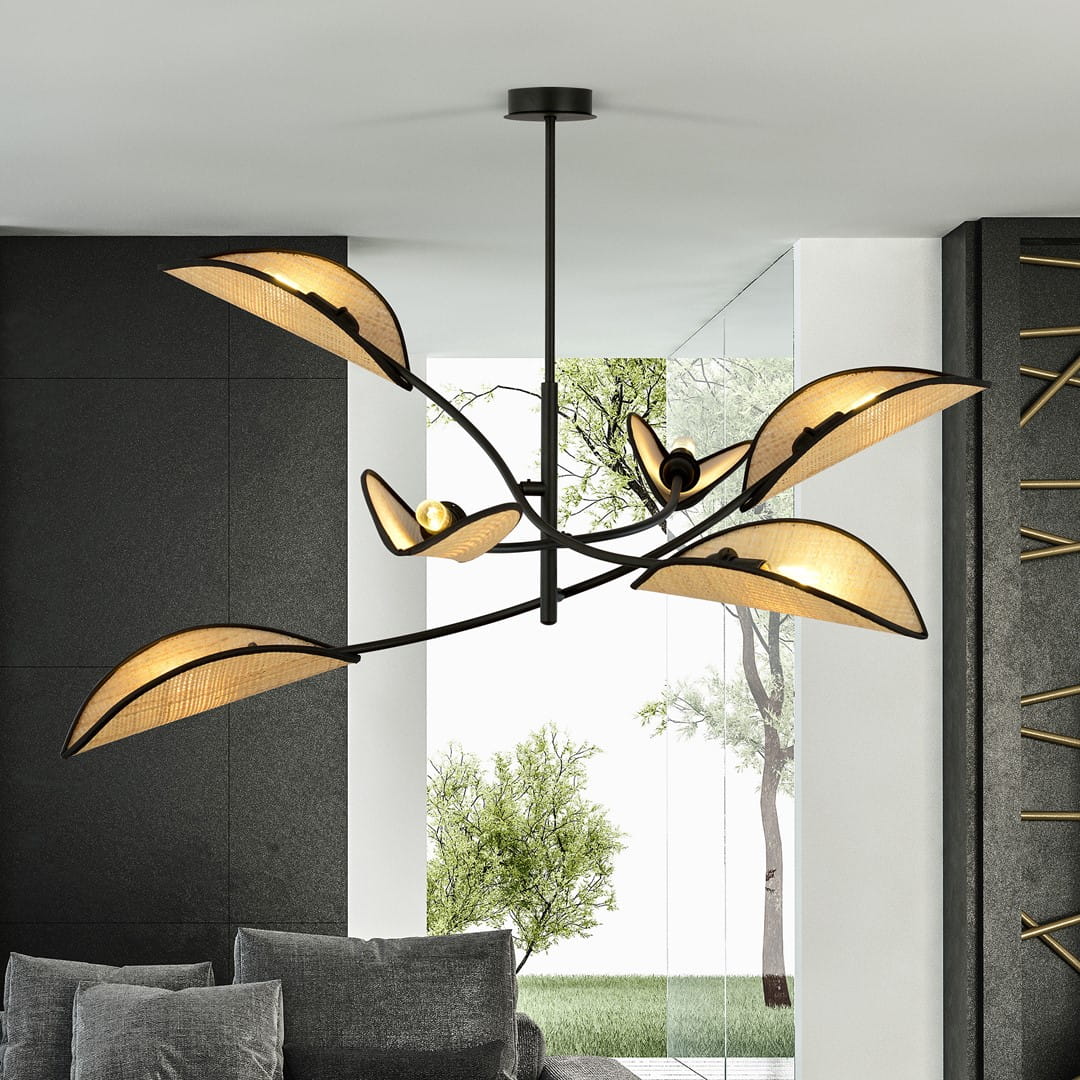 Lampa sufitowa Lotus 6-punktowa w kolorze czarnym z rattanowymi kloszami w kształcie liści. Ujęcie z dołu, zawieszona na cienkim metalowym stelażu. W tle widoczna zieleń przez duże okno, a sofa w odcieniach szarości.