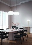 Lampa wisząca Fomento D40 z mosiężnymi detalami i białym kloszem, zawieszona nad okrągłym stołem w eleganckiej jadalni. W tle widoczne czarne krzesła, szklane naczynia i dekoracyjne gałązki. Jasne, neutralne tło wnętrza.