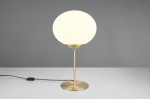 Lampa stołowa Fomento z mosiężną podstawą i białym, okrągłym kloszem. Ujęcie frontalne, lampa stoi na białym blacie. Widoczny czarny kabel z przełącznikiem. Prosta forma, eleganckie wykończenie.