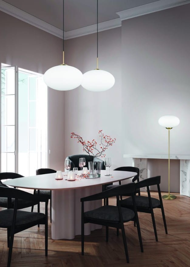Lampa podłogowa Fomento z mosiężną nogą i białym kloszem, ustawiona w rogu nowoczesnego wnętrza. Produkt ma prostą, elegancką formę i jest złożony, co podkreśla minimalistyczny styl aranżacji.
