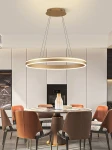 Lampa wisząca Vivies 1xLED/36W w kolorze złotym, o okrągłym kształcie, zawieszona na cienkich linkach. Widoczna w kuchni nad okrągłym stołem, w jasnym otoczeniu z nowoczesnymi meblami.