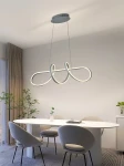 Lampa wisząca Trevance 1xLED/56W w kolorze szarym, o nowoczesnym, organicznym kształcie, zawieszona na cienkich linkach. Umieszczona nad okrągłym stołem w jasnym wnętrzu, z roślinnością w tle.