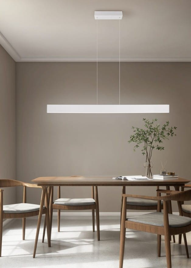 Lampa wisząca Galway w kolorze szarym z jednym źródłem LED o mocy 35W, zawieszona nisko nad drewnianym stołem w minimalistycznym wnętrzu. Lampa ma prostokątny kształt i jest zawieszona na cienkich linkach. W tle widać zieloną roślinę w doniczce.