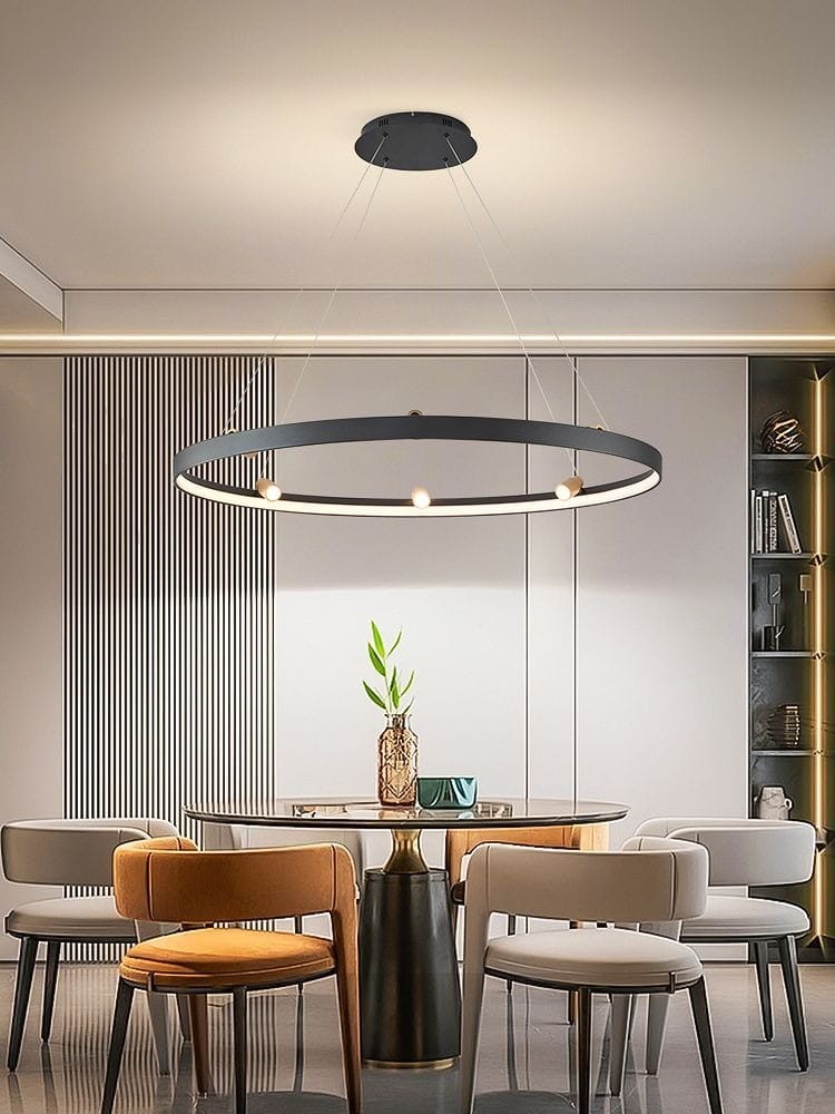 Lampa wisząca Pignano z 7 żarówkami LED, o mocy 54W, w kolorze czarnym i złotym. Okrągły kształt, zawieszona na cienkich linkach, umieszczona nad okrągłym stołem w nowoczesnej aranżacji. Tło z jasnymi ścianami i meblami.