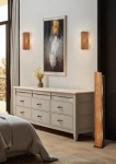 Lampa podłogowa Karuni 1xE27 w kolorze czarnym z jasnym drewnem, stojąca obok komody w jasnym wnętrzu. Gładka, prostokątna podstawa, z przezroczystym kloszem, emituje ciepłe światło, tworząc przytulną atmosferę.
