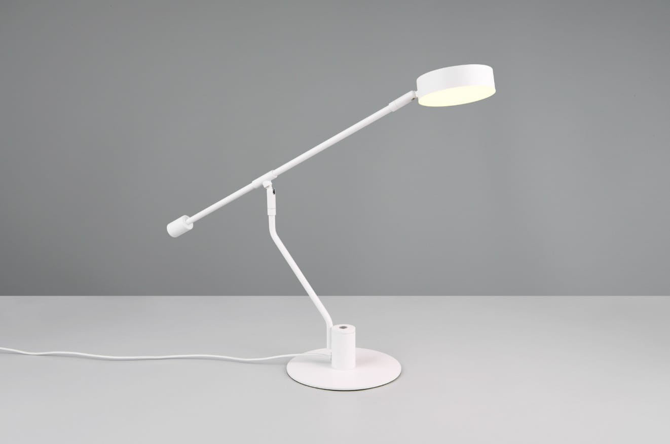 Lampa biurkowa Manduro w kolorze białym z LED o mocy 6W. Posiada regulowane ramię i okrągłą podstawę. Ujęcie z boku, ukazujące lampę w pozycji stojącej na szarej powierzchni. Kabel zasilający widoczny w dolnej części.