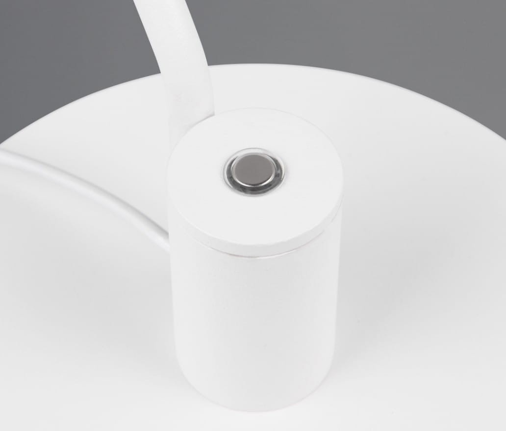 Biała lampa biurkowa Manduro z wbudowanym źródłem LED 6W. Ujęcie z góry na cylindryczną podstawę z przyciskiem włączającym umieszczonym na górze. Gładka, matowa powierzchnia, z białym kablem elektrycznym.