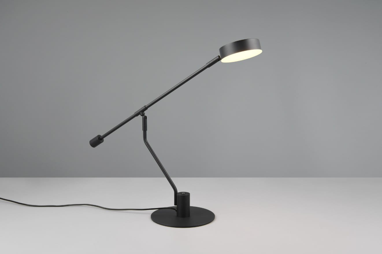 Czarna lampa biurkowa Manduro z regulowanym ramieniem, wyposażona w 1 diodę LED o mocy 6W. Stojąca na okrągłej podstawie, z okrągłym kloszem, emitującym ciepłe światło. Ujęcie z boku, na jednolitym tle.