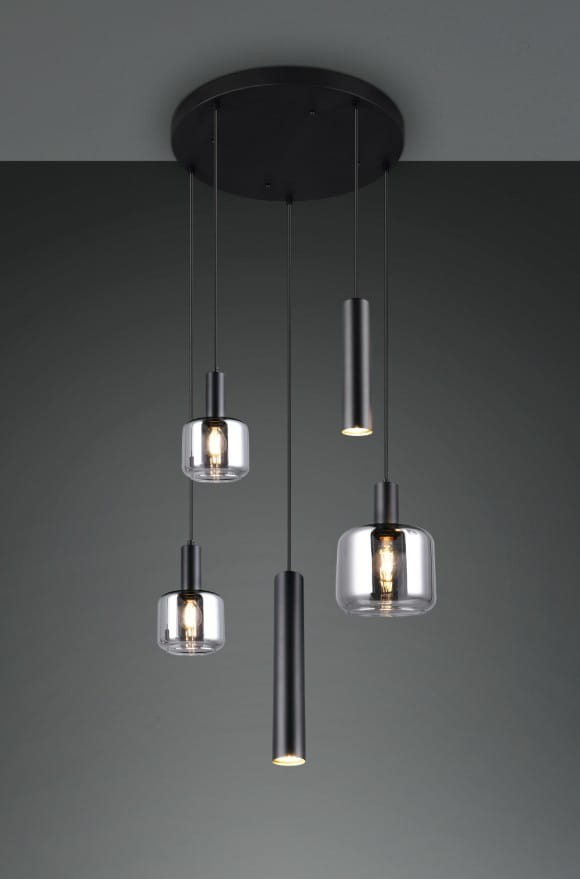 Czarna lampa wisząca Mataro z pięcioma źródłami światła w różnych kształtach: dwa cylindryczne, jeden okrągły z przezroczystym kloszem oraz dwa długie metalowe. Lampa zawieszona na cienkich linkach, montowana do sufitu, na tle szarej ściany.