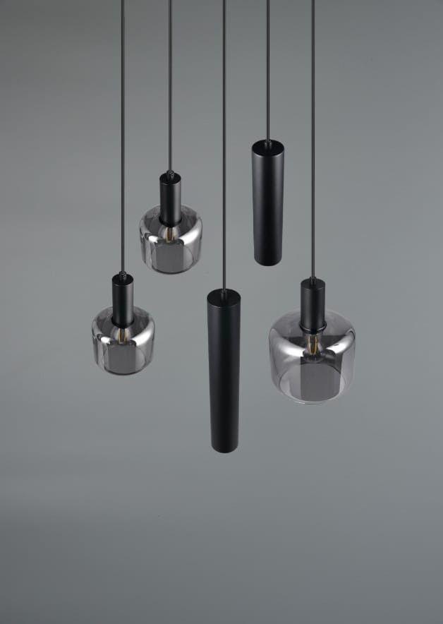 Lampa wisząca Mataro z pięcioma źródłami światła, w kolorze czarnym. Składa się z dwóch okrągłych, przezroczystych kloszy oraz trzech prostokątnych, czarnych elementów. Zawieszona na cienkich linkach, na szarym tle.