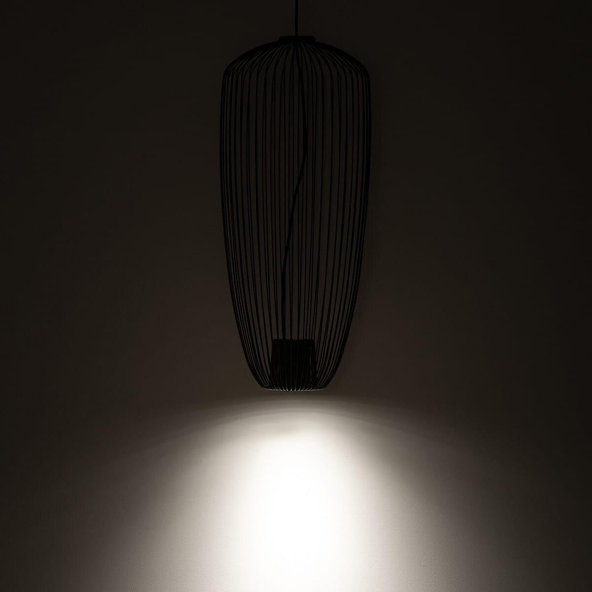 Lampa wisząca Pumpkin S w kolorze szarym z metalową konstrukcją w formie siatki. Zawieszona na cienkim przewodzie, emitująca światło w dół. Widoczny detal na ścianie, tworzący delikatny efekt świetlny.