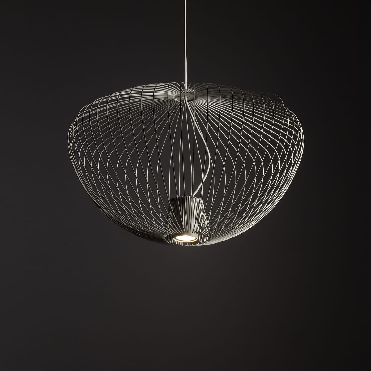 Lampa wisząca Pumpkin M w jasnoszarym kolorze, wykonana z cienkich metalowych drutów, ma okrągły kształt. Widoczny jest gniazdko na żarówkę GU10. Ujęcie z dołu, na jednolitym ciemnym tle, podkreśla nowoczesny design lampy.