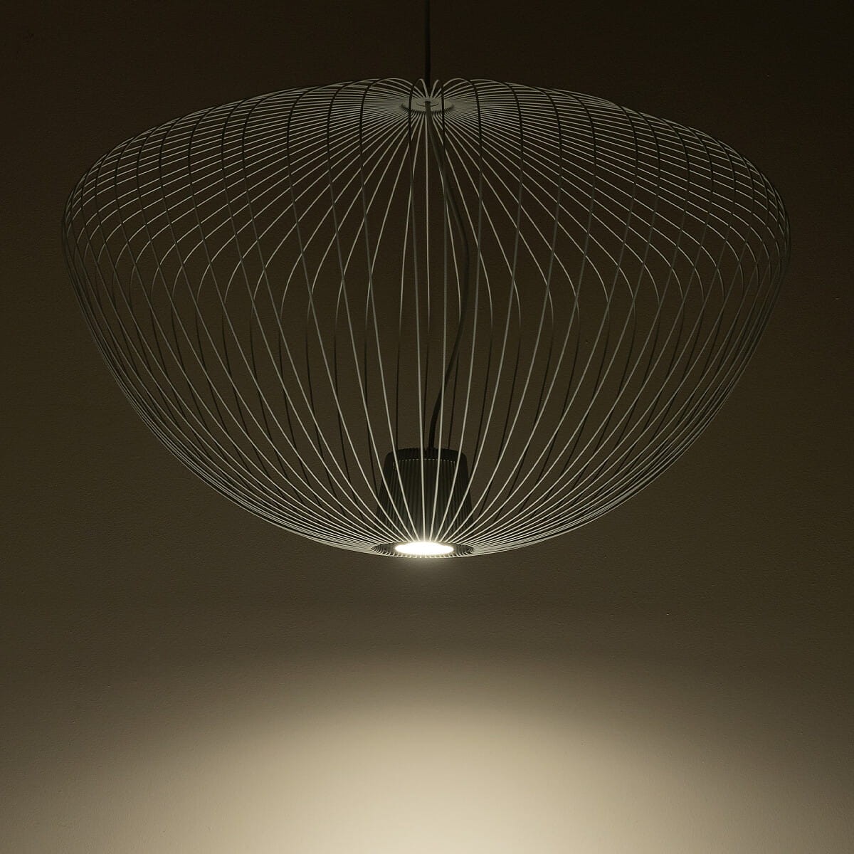 Lampa wisząca Pumpkin L w kolorze jasnoszarym z metalowej siatki. Okrągły kształt z otwartą dolną częścią, z widocznym źródłem światła GU10. Wisi na cienkim przewodzie, a tło jest ciemne, co podkreśla jej subtelny design.