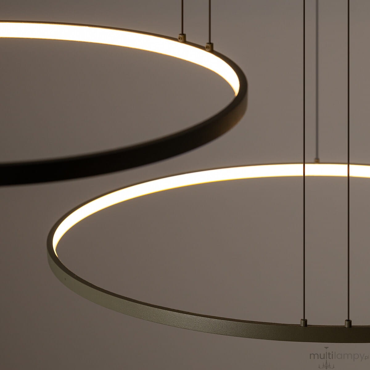 Lampa wisząca Circolo D125 w kolorze oliwkowym z trzema źródłami światła LED o mocy 45W i temperaturze 3000K. Posiada dwa okrągłe, metalowe pierścienie zawieszone na cienkich linkach, emitujące ciepłe światło.