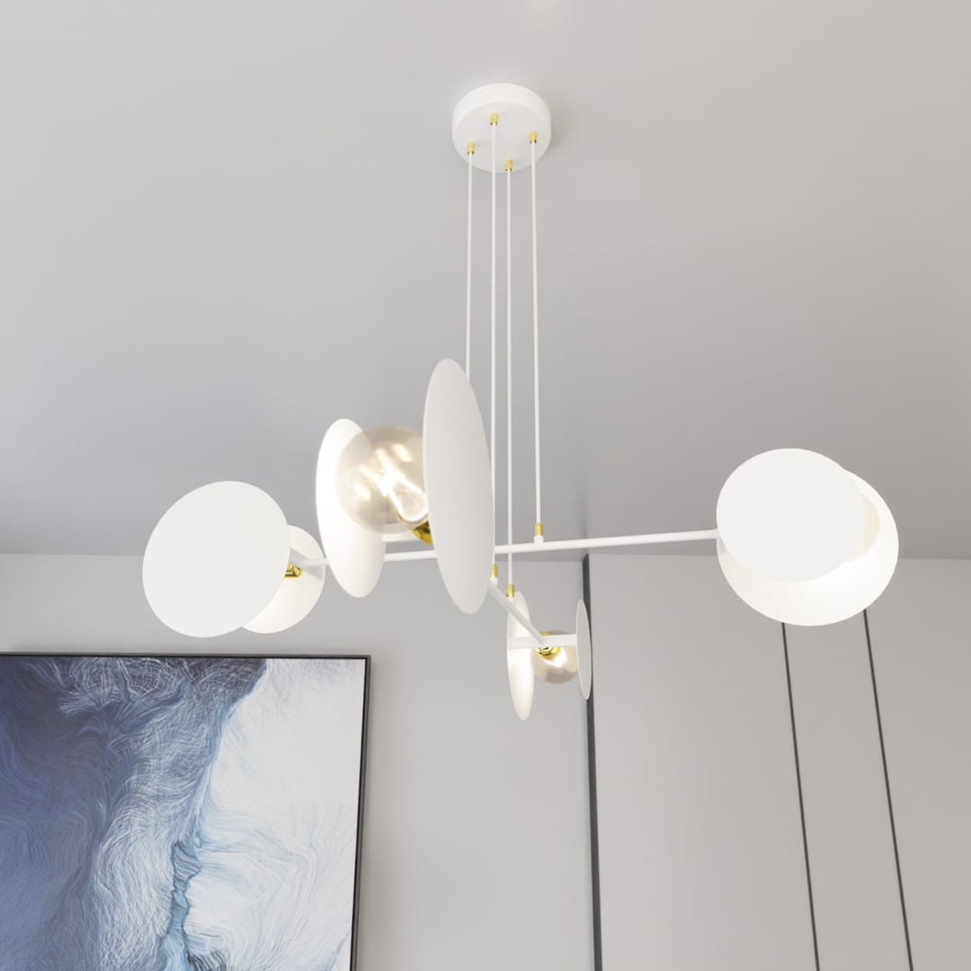 Lampa wisząca Idea 4-punktowa w kolorze białym z okrągłymi kloszami w złotych detalach. Zawieszona na cienkich linkach, z centralnym mocowaniem sufitowym. Widoczna w nowoczesnym wnętrzu z obrazem w tle.