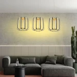Lampa wisząca Xara z trzema źródłami LED, w kolorze czarnym z elementami złotymi. Oświetlenie ma nowoczesny design, zawieszona w rzędzie nad szaro-zieloną sofą, na tle jasnej, surowej ściany.
