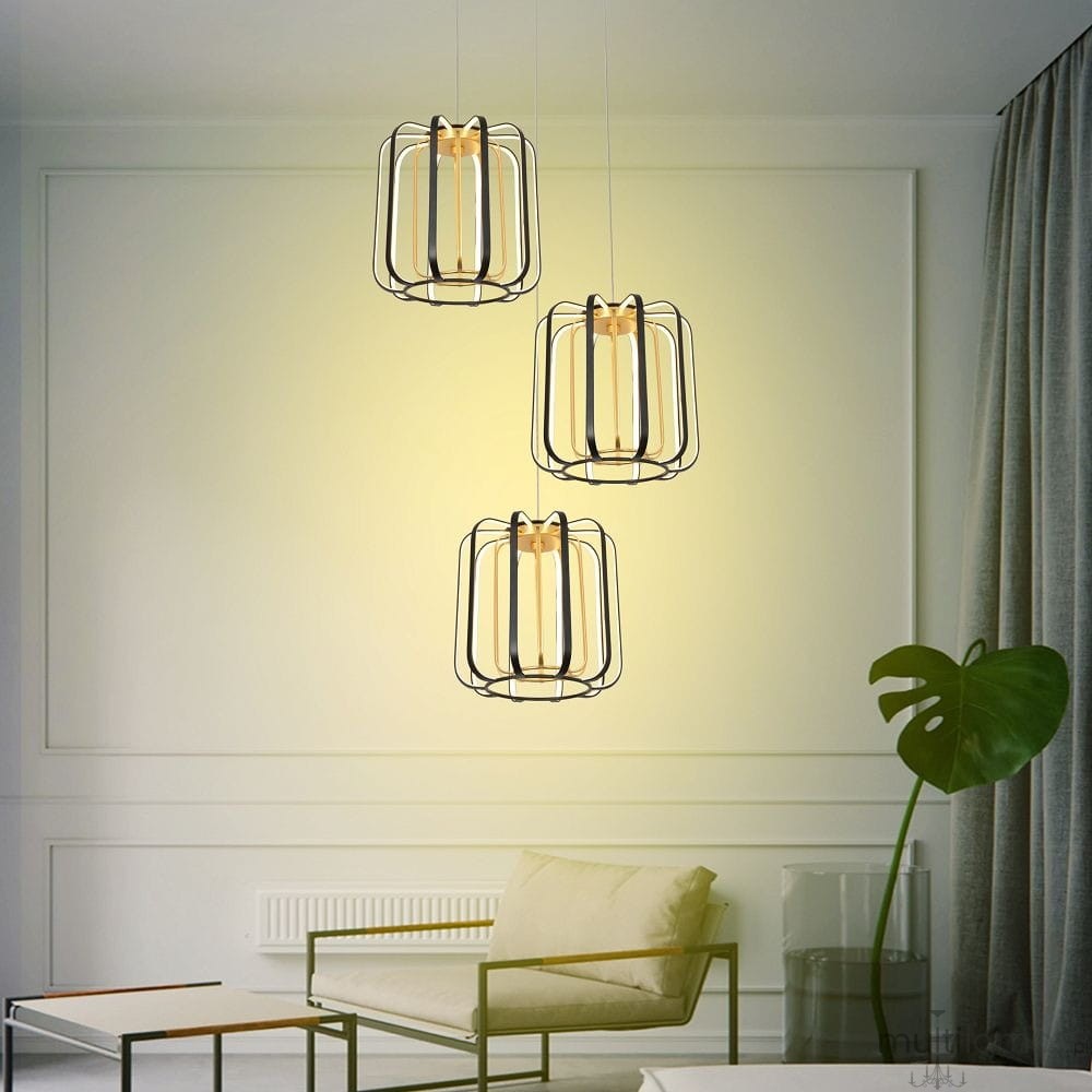 Lampa wisząca Xara, czarna z złotymi akcentami, z trzema kloszami LED. Klosze mają metalową siatkę, wisi w eleganckim wnętrzu obok rośliny. Oświetlenie emitowane jest w ciepłej tonacji, tworząc przytulną atmosferę.