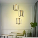 Lampa wisząca Xara, czarna z złotymi akcentami, z trzema kloszami LED. Klosze mają metalową siatkę, wisi w eleganckim wnętrzu obok rośliny. Oświetlenie emitowane jest w ciepłej tonacji, tworząc przytulną atmosferę.