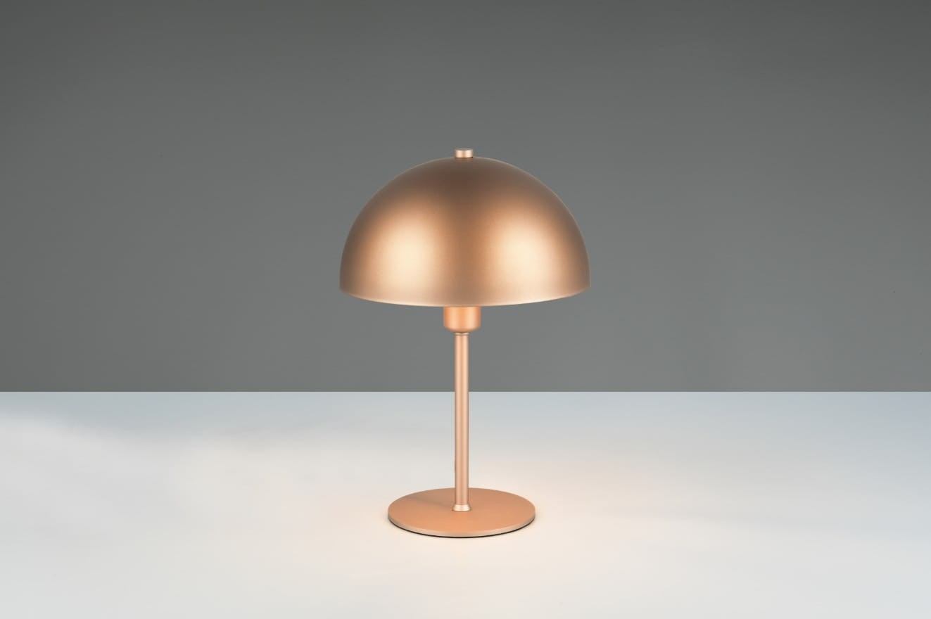 Lampa stołowa Nola w kolorze kawowym, z metalowym kloszem o półkulistym kształcie i prostym, cylindrycznym stelażu. Ujęcie frontalne, produkt stoi na płaskiej powierzchni, w tle jednolity kolor. Pasuje do nowoczesnych wnętrz.
