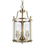 Lampa wisząca New York w kolorze mosiądzu, z przezroczystym kloszem, posiada trzy źródła światła E14. Okrągła podstawa z detalami w kształcie świeczników, zawieszona na łańcuchu, prezentowana z przodu.