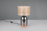 Lampa stołowa Tara z chromowaną podstawą o zaokrąglonym kształcie i naturalnym abażurem z plecionej tkaniny. Produkt stoi na gładkiej powierzchni, z widocznym przewodem zasilającym. Wysokość abażuru podkreśla jego teksturę.