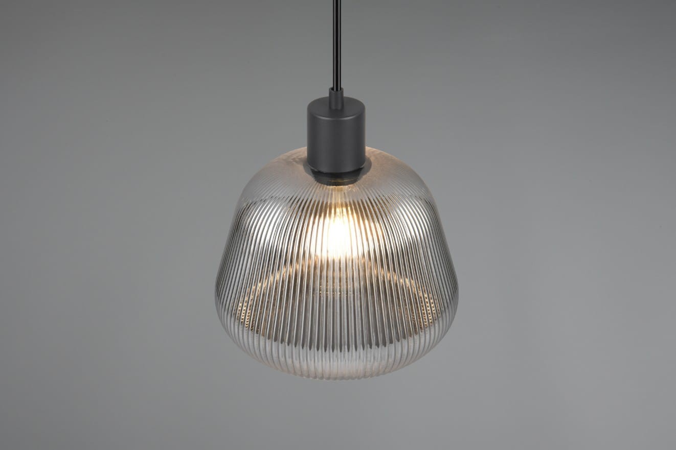Lampa wisząca Tarifa z kloszem w formie szklanej, przezroczystej kopuły z wyraźnym prążkowaniem. Posiada czarny uchwyt i miejsce na żarówkę E27. Zawieszona w górnej części, na jednolitym tle.