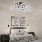 Lampa sufitowa Tarifa w kolorze czarnym z sześcioma miejscami na żarówki E14. Ujęcie z góry, zawieszona w sypialni, w otoczeniu dwóch obrazów na ścianie oraz lamp nocnych obok łóżka.