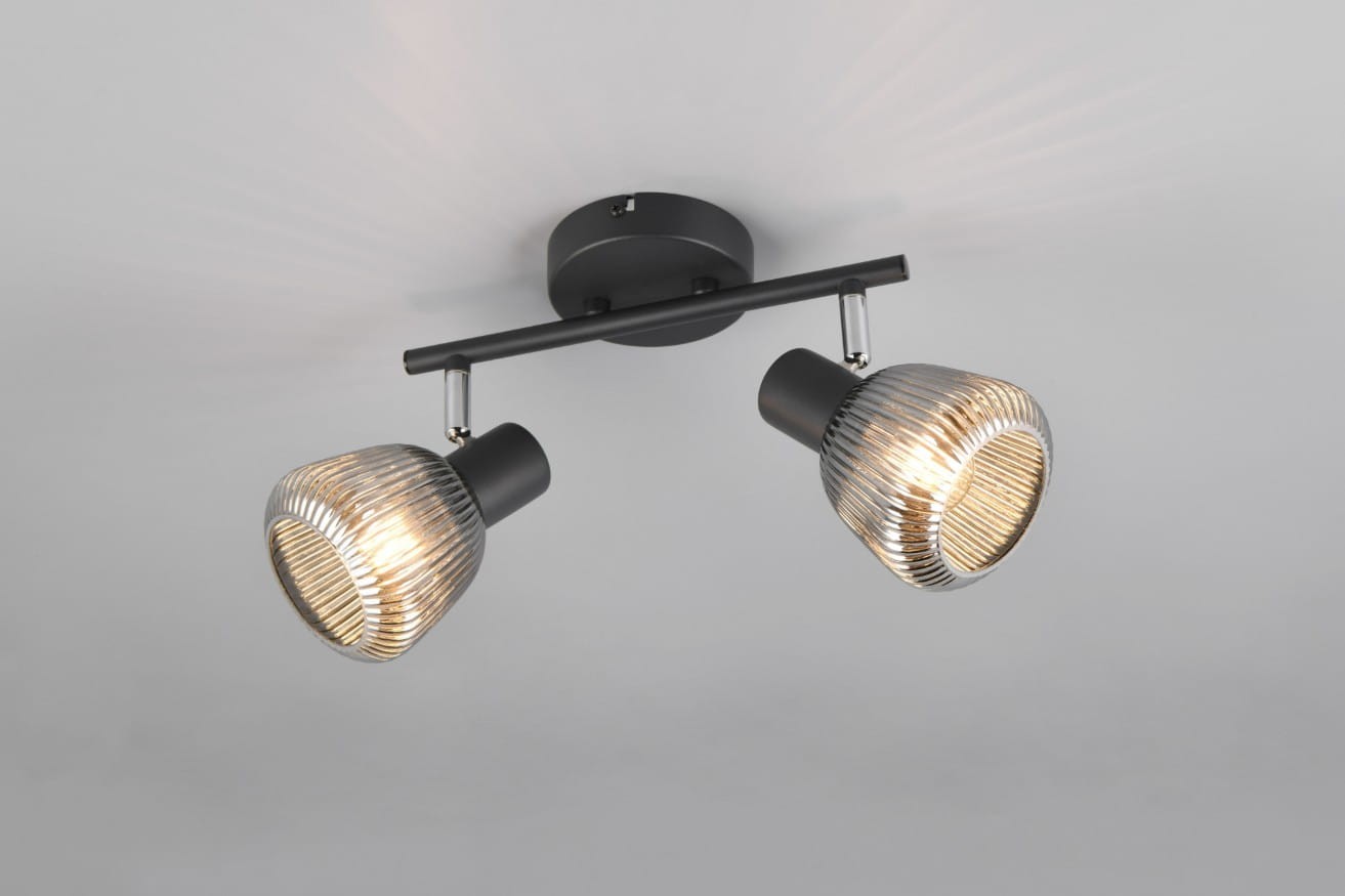 Lampa sufitowa Tarifa w kolorze czarnym z dwiema oprawami E14. Zawieszona na metalowej rurze, z kloszami w formie żarówek o żłobieniach, emitującymi ciepłe światło. Kąt ujęcia zbliżony na sufit, prezentujący szczegóły konstrukcji.