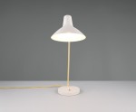 Lampa stołowa Traveller w kolorze szarym i złotym, z podstawą z białego materiału i złotą metalową nogą. Posiada klosz w kształcie stożka, emitujący ciepłe światło. Ujęcie frontalne, widoczny kabel zasilający w żółtym kolorze.
