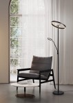 Czarna lampa podłogowa Willis z dwoma źródłami LED (44,5W) i regulowanym ramieniem. Stoi obok szarego fotela i białego stolika kawowego, w tle duże okno z zasłonami. Wyróżnia się nowoczesnym designem i okrągłym kloszem.