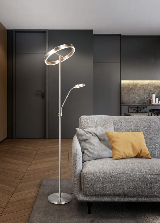 Lampa podłogowa Willis w kolorze niklowym, z dwoma źródłami światła LED. Posiada okrągłą górną część i elastyczne ramię, stojąca obok szarej sofy z poduszkami. Tło w odcieniach szarości i drewna, nowoczesne wnętrze.