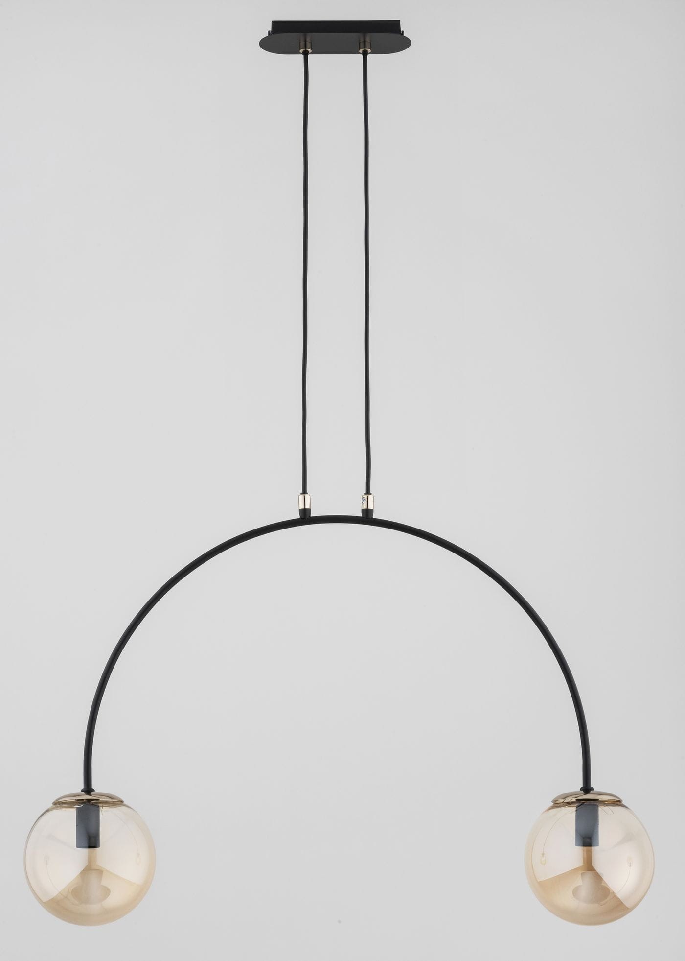 Lampa wisząca Bendo mix 2xE14 w czarno-złotej kolorystyce. Posiada dwa okrągłe klosze w przezroczystym odcieniu, zawieszone na czarnym, łukowatym stelażu. Zawieszenie na dwóch czarnych przewodach. Tło jasne, jednolite.