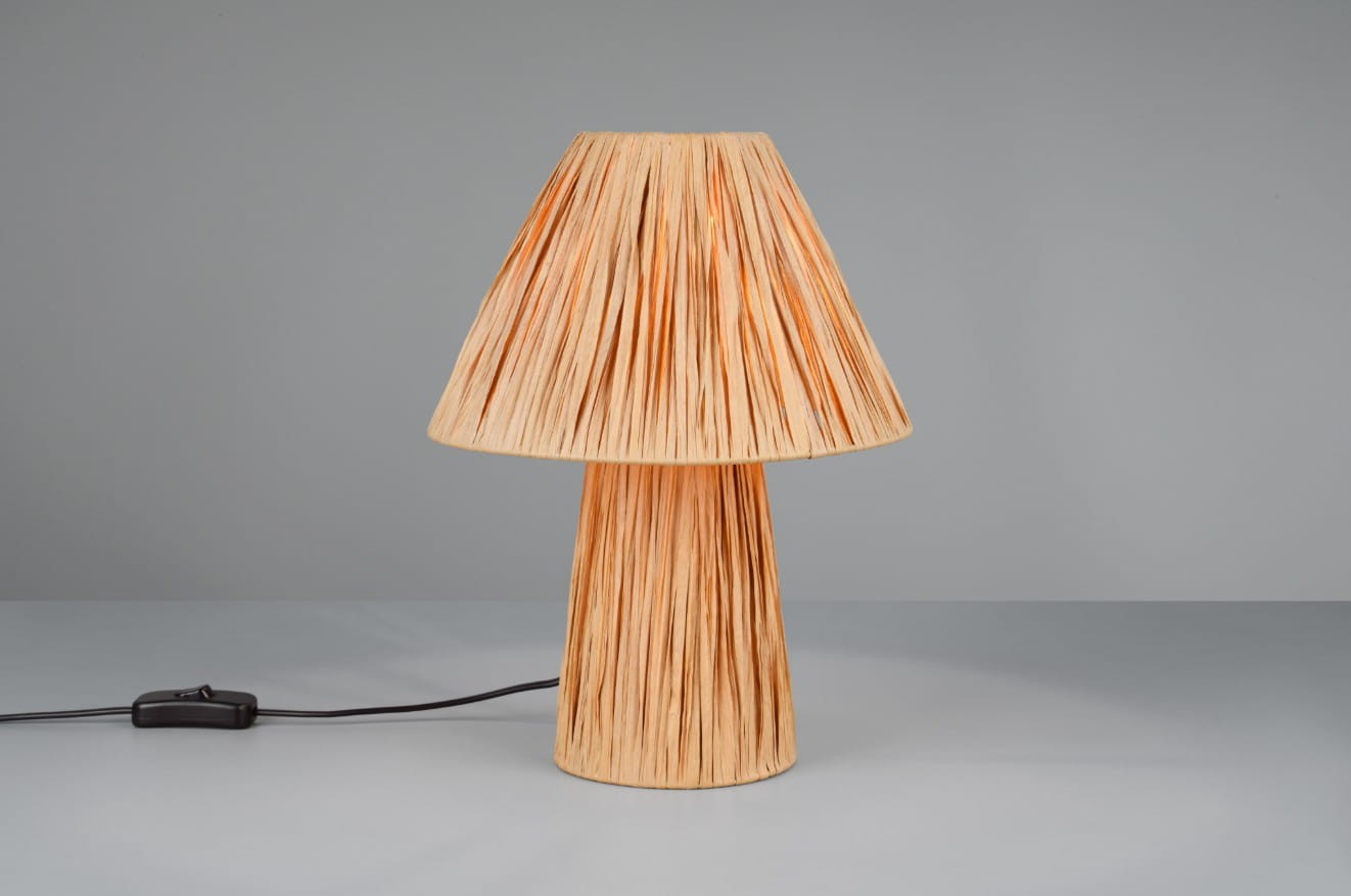 Brązowa lampa stołowa Anea z abażurem w formie stożka, wykonana z materiału o teksturowanej powierzchni. Ustawiona pionowo na płaskiej powierzchni, z przewodem elektrycznym widocznym z boku. Tło w odcieniu szaro-beżowym.