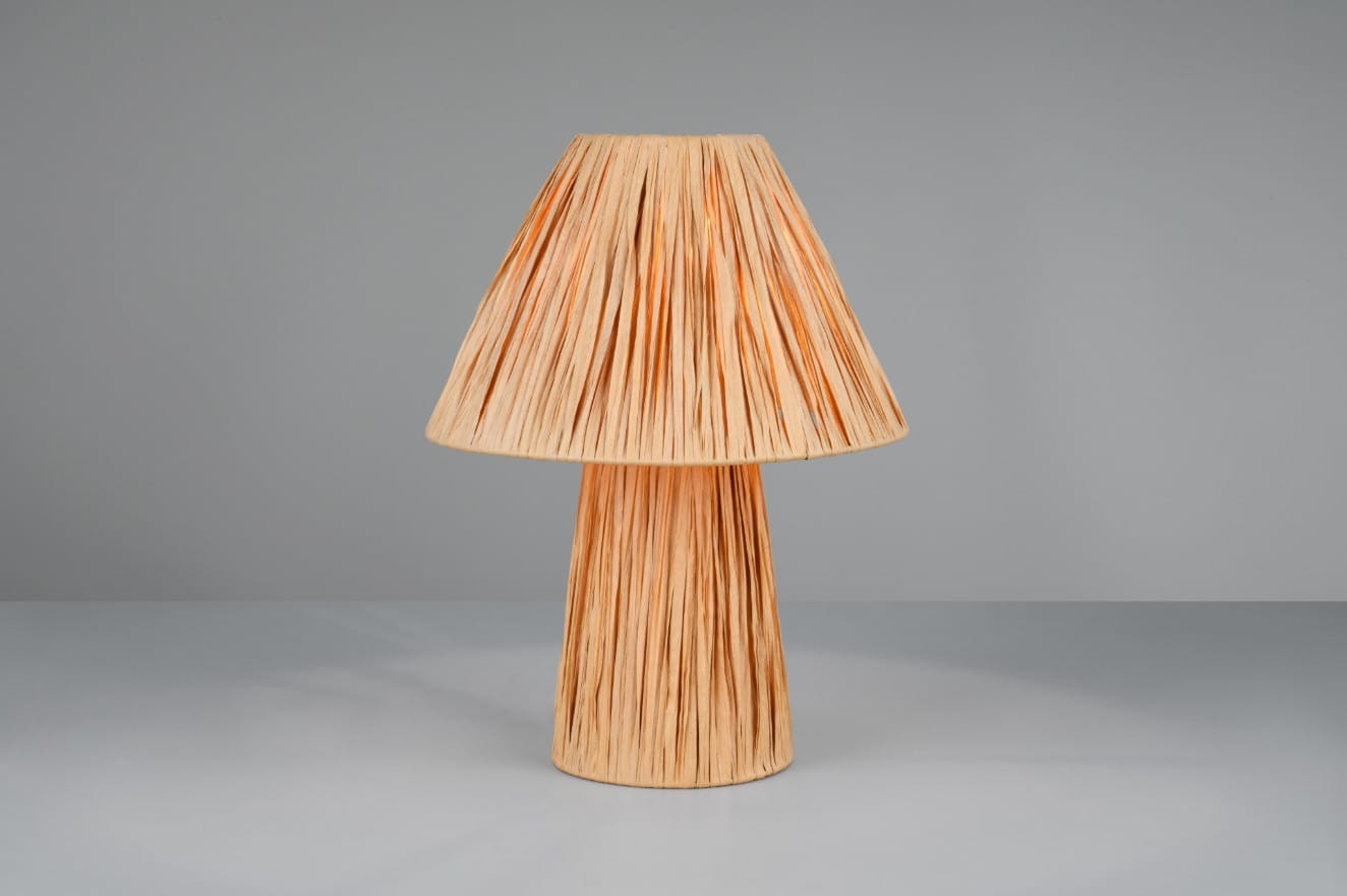 Lampa stołowa Anea w brązowym kolorze z kloszem w formie stożka i fakturą przypominającą plecionkę. Ustawiona na płaskiej powierzchni, z widocznym miejscem na żarówkę E27. Tło jednolite, szare.