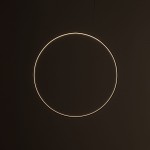 Lampa wisząca Circolo D60 o okrągłym kształcie, wykonana z materiału w kolorze oliwkowym, z jedną diodą LED 21W, emitującą światło o temperaturze 3000K. Zawieszona na cienkich linkach, na ciemnym tle.