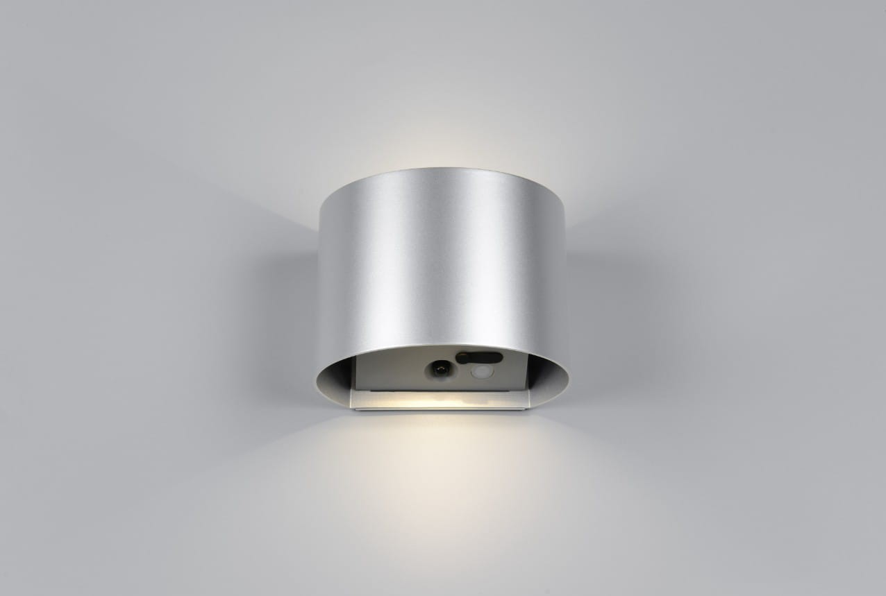 Kinkiet zewnętrzny Genie w kolorze tytanowym, cylindryczny kształt, z wbudowanym czujnikiem ruchu. Oświetlenie LED (2x2W) emituje jasne światło, montowane na ścianie, z widocznym czujnikiem i przyciskiem. Stopień ochrony IP44.