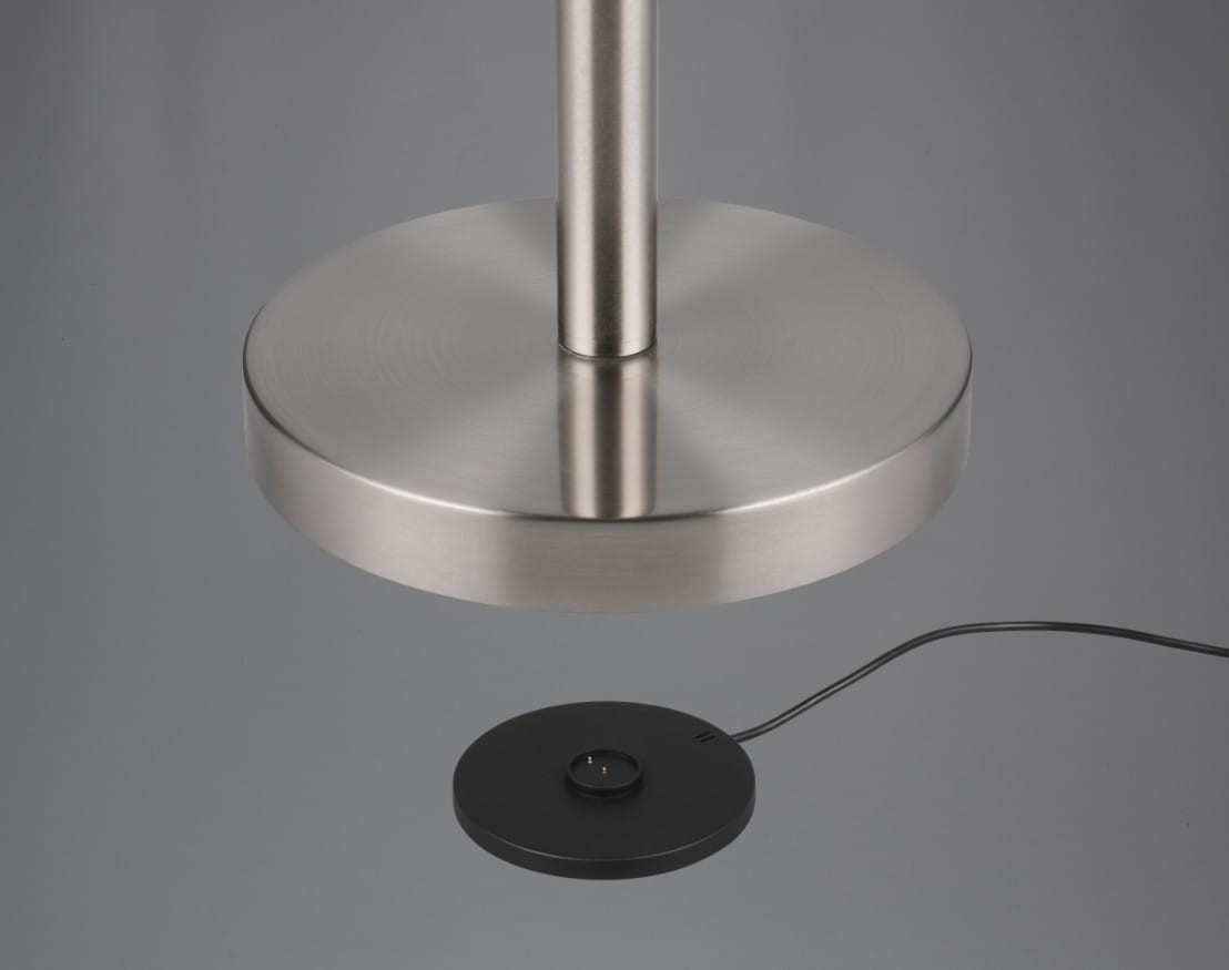 Lampa podłogowa Gomez w kolorze tytanowym, bezprzewodowa, z jedną diodą LED 3W. Widoczna okrągła podstawa z matowego metalu oraz czarna płytka ładująca z kablem. Produkt ustawiony w pozycji stojącej, z detalem na podstawie i górnej części lampy.