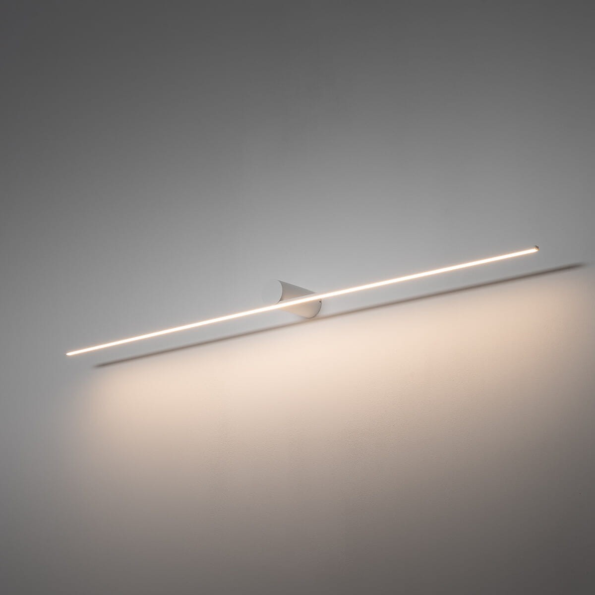 Biały kinkiet Spin 120 z jedną diodą LED o mocy 16W i temperaturze barwowej 3000K. Zamontowany na ścianie, ma minimalistyczny, prosty design z cienką linią światła oraz zaokrąglonym uchwytem. Tło w jasnym kolorze.
