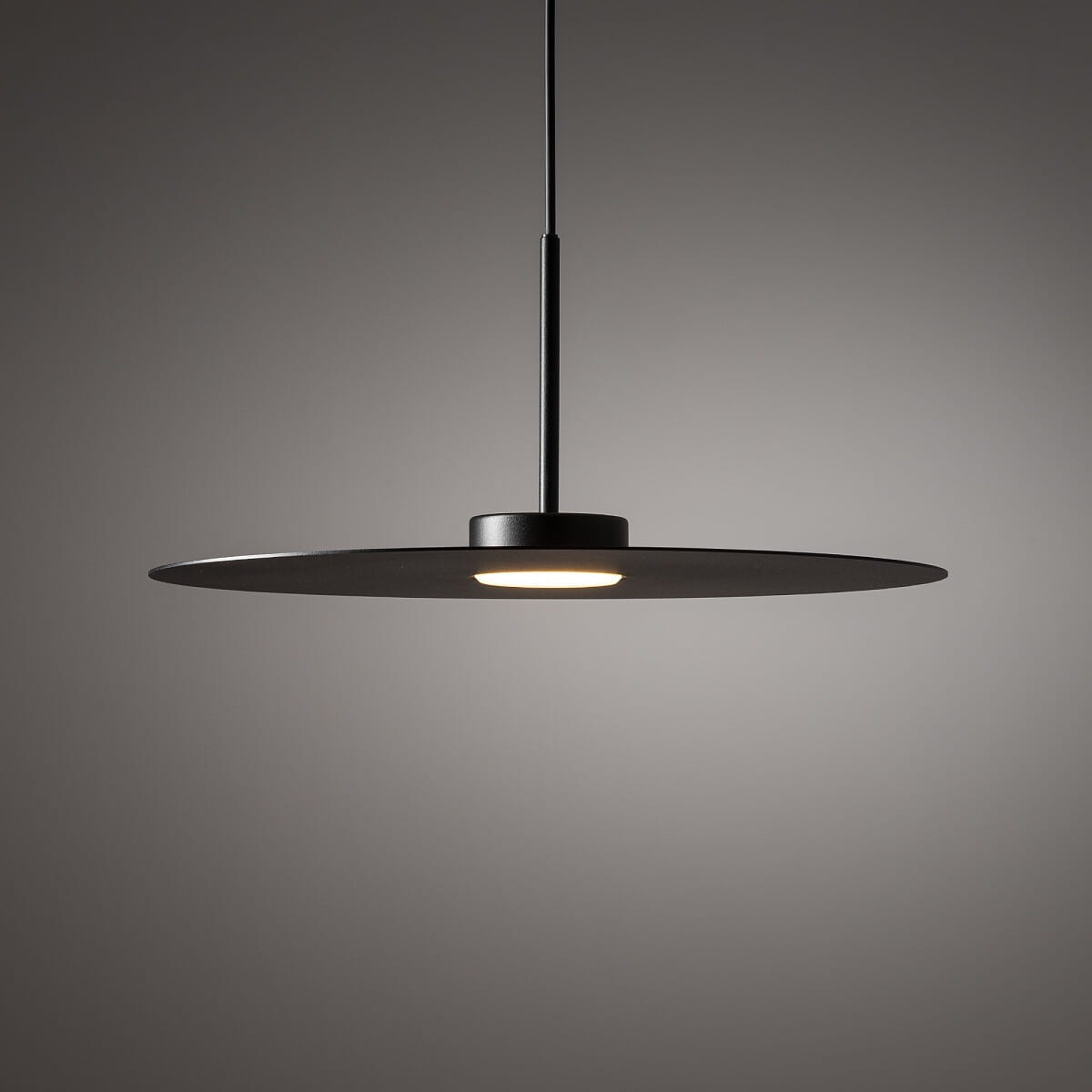 Lampa wisząca Simone w kolorze czarnym z okrągłym, płaskim kloszem i pojedynczym źródłem światła GX53. Produkt zawieszony na cienkim drucie, prezentowany w neutralnym tle, co podkreśla jego nowoczesny design.