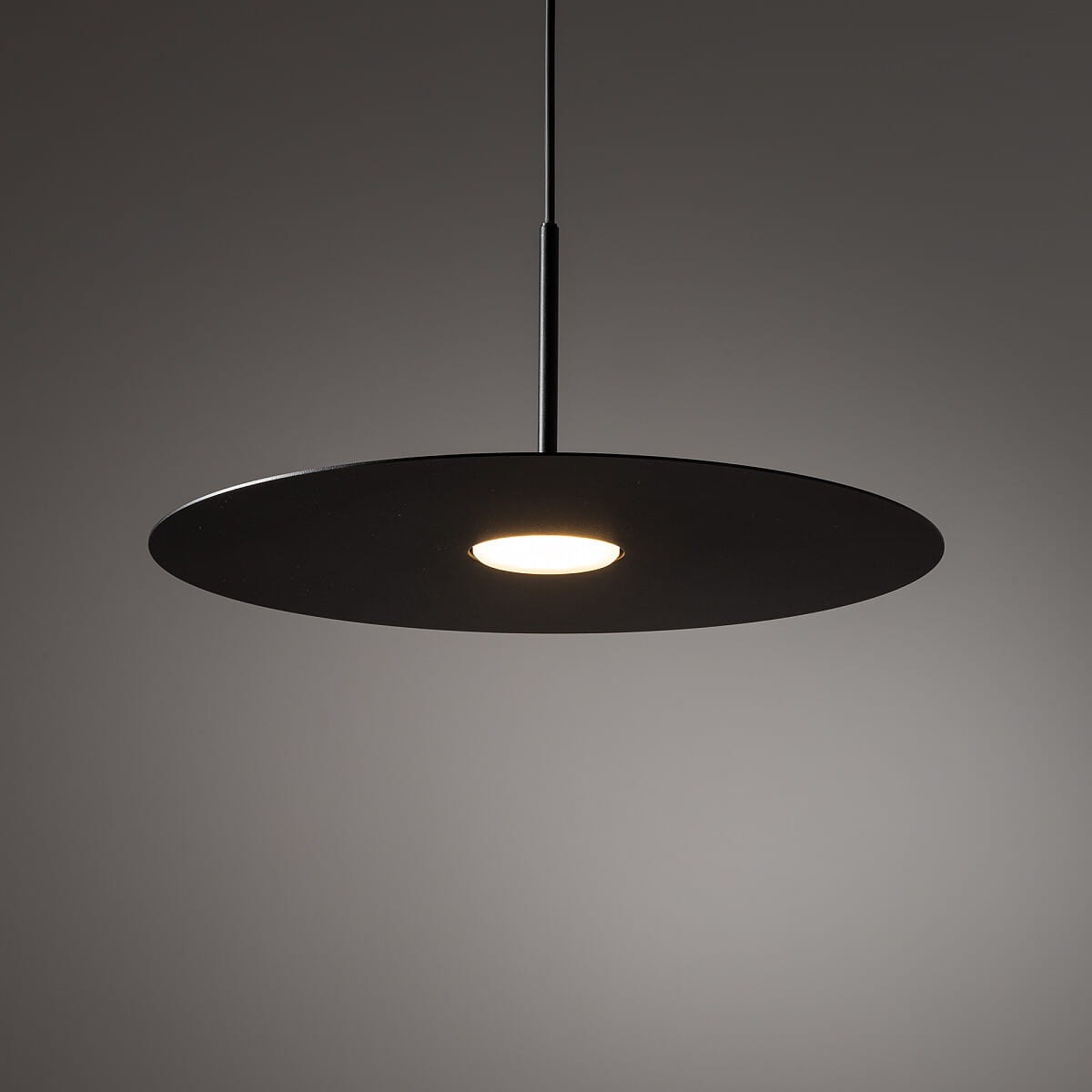 Czarna lampa wisząca Simone z jednym źródłem światła GX53. Okrągła, matowa czasza z centralnym otworem na żarówkę, zawieszona na cienkim przewodzie. Prosta forma, idealna do nowoczesnych wnętrz.